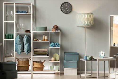 Neatly organized modern living room shelving with rolled towels, folded blankets, decorative baskets, and color-coordinated storage boxes by professional home organizers