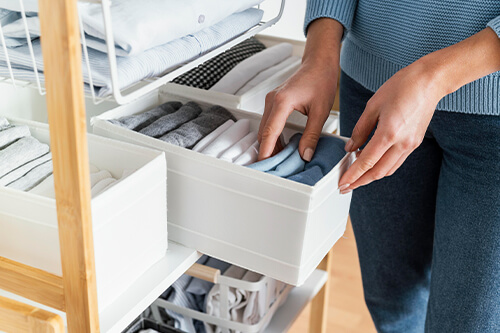 Professional closet organization with neatly folded clothes and color-coordinated rolled socks in white drawer organizers